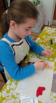 Young girl sewing felt shapes onto a fabric background at Tuftydawn Designs studio.